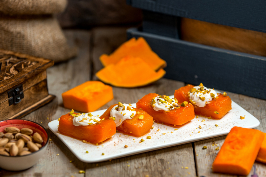 Sweet potato dessert squares topped with cream and nuts on a white plate
